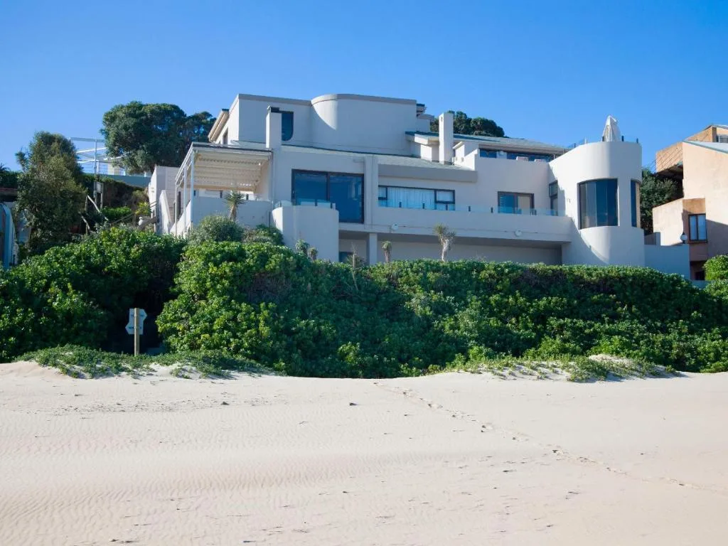 Modern white beachfront apartment building with blue-framed windows overlooking sandy beach