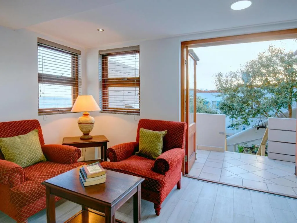 Bright lounge with red patterned armchairs, coffee table, and water view doors
