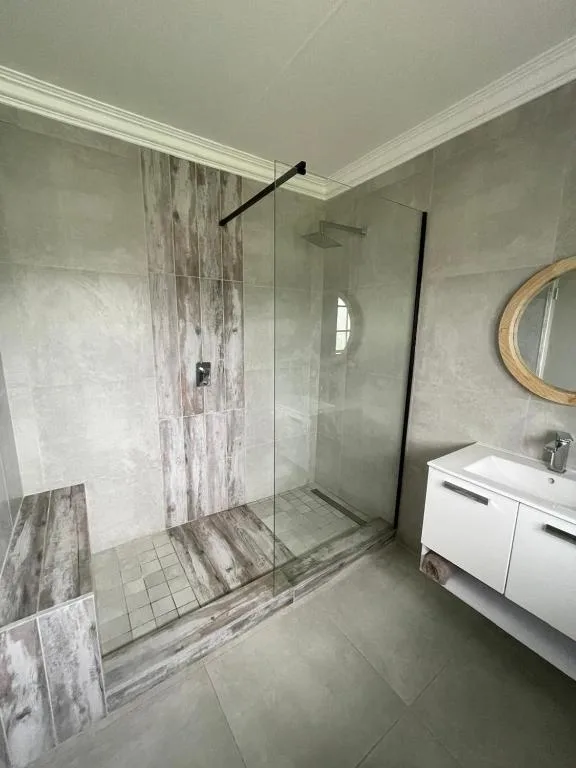 Modern bathroom with walk-in shower, white vanity, and circular mirror