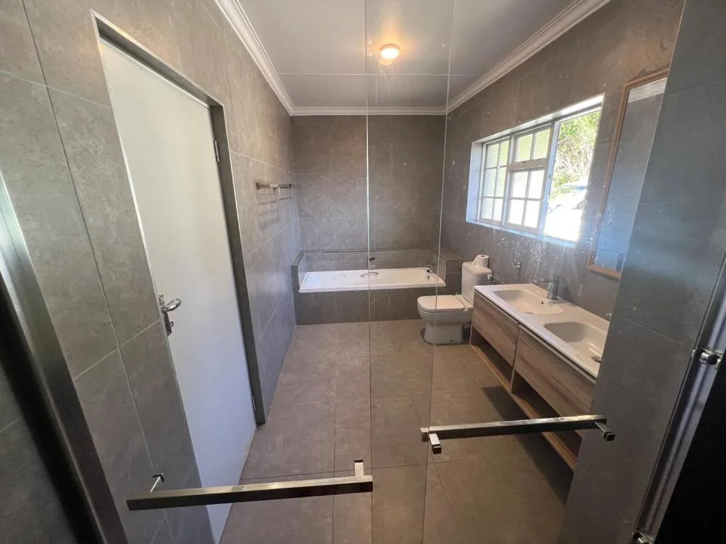 Modern bathroom with walk-in shower, dual vanity, and natural light from window