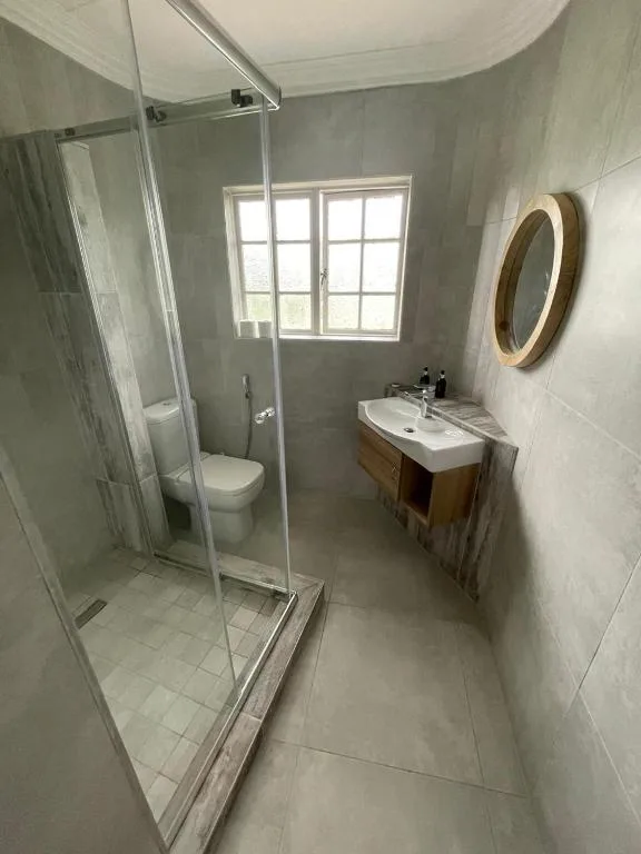 Modern bathroom with glass shower enclosure, wooden vanity, round mirror, and window