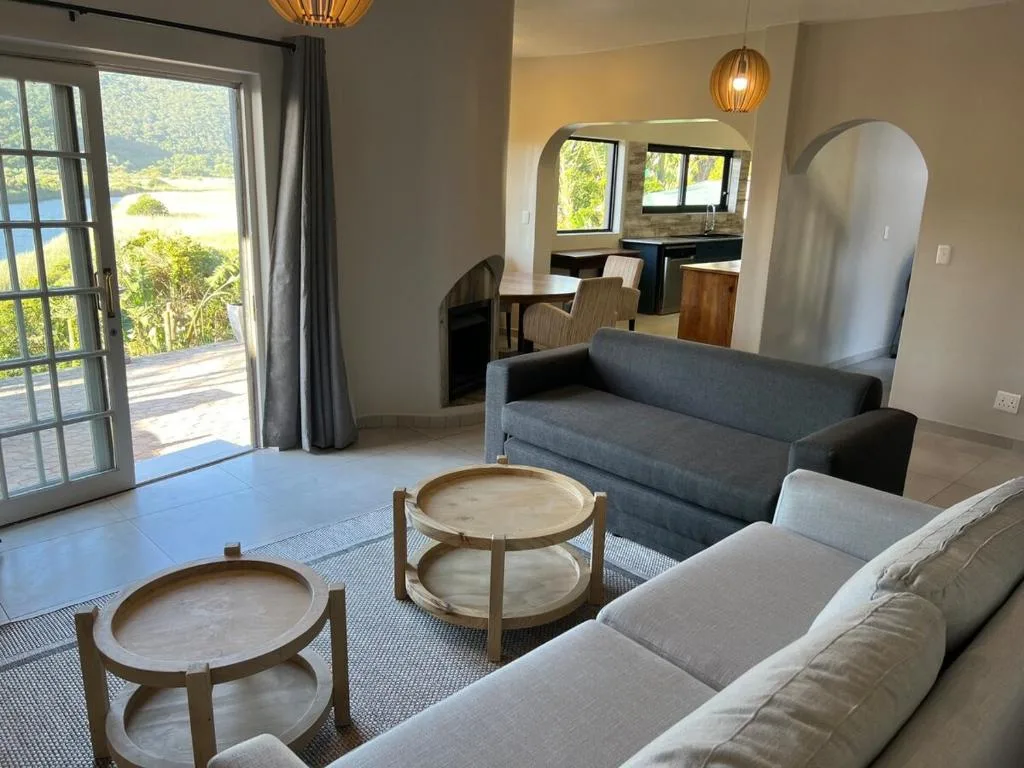 Spacious open-plan lounge with gray sofas, wooden side tables, and lagoon views through glass doors