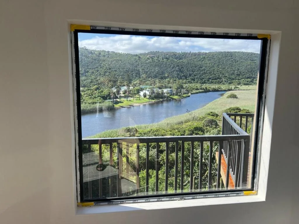 Scenic lagoon and forested hillside vista framed by railing and window