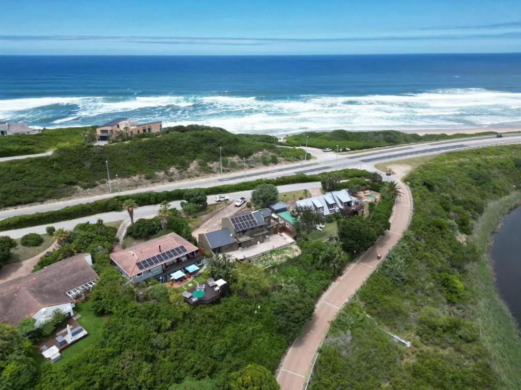 Aerial view of coastal property with ocean, beach, and green surroundings