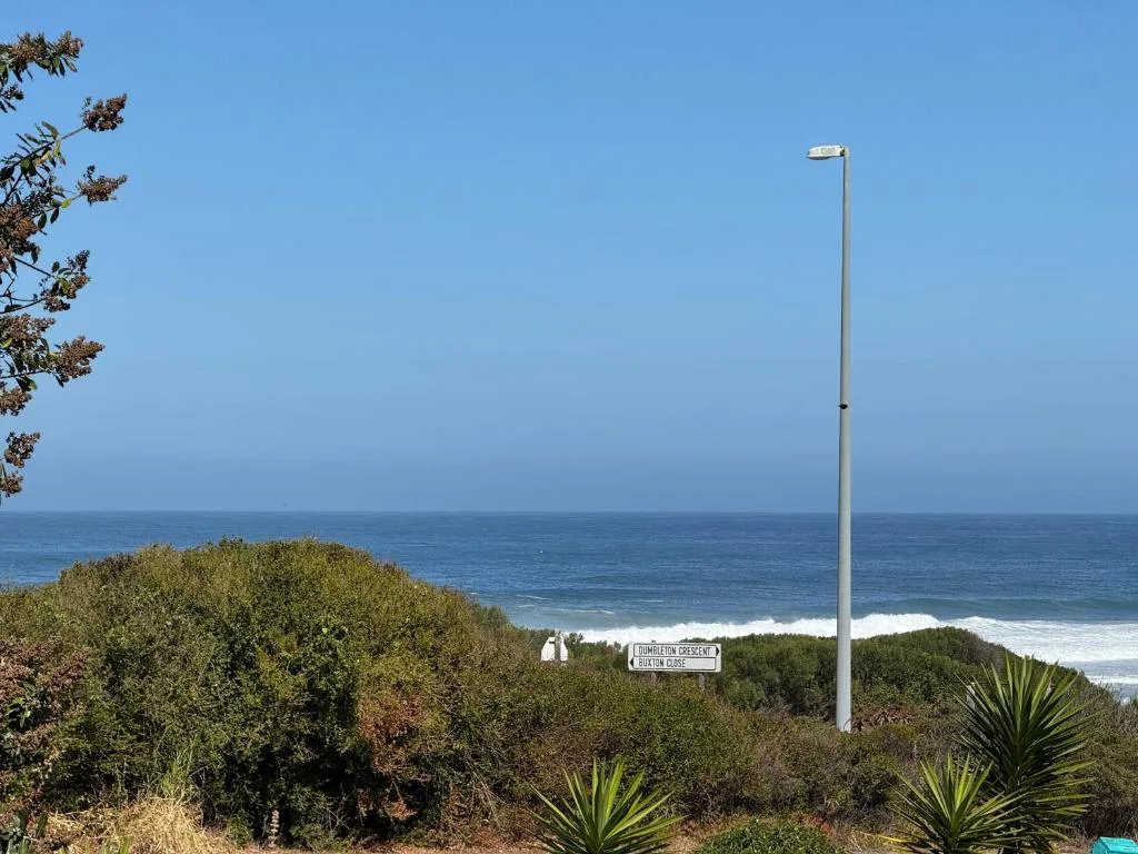 Ocean view from property with coastal vegetation and street sign visible