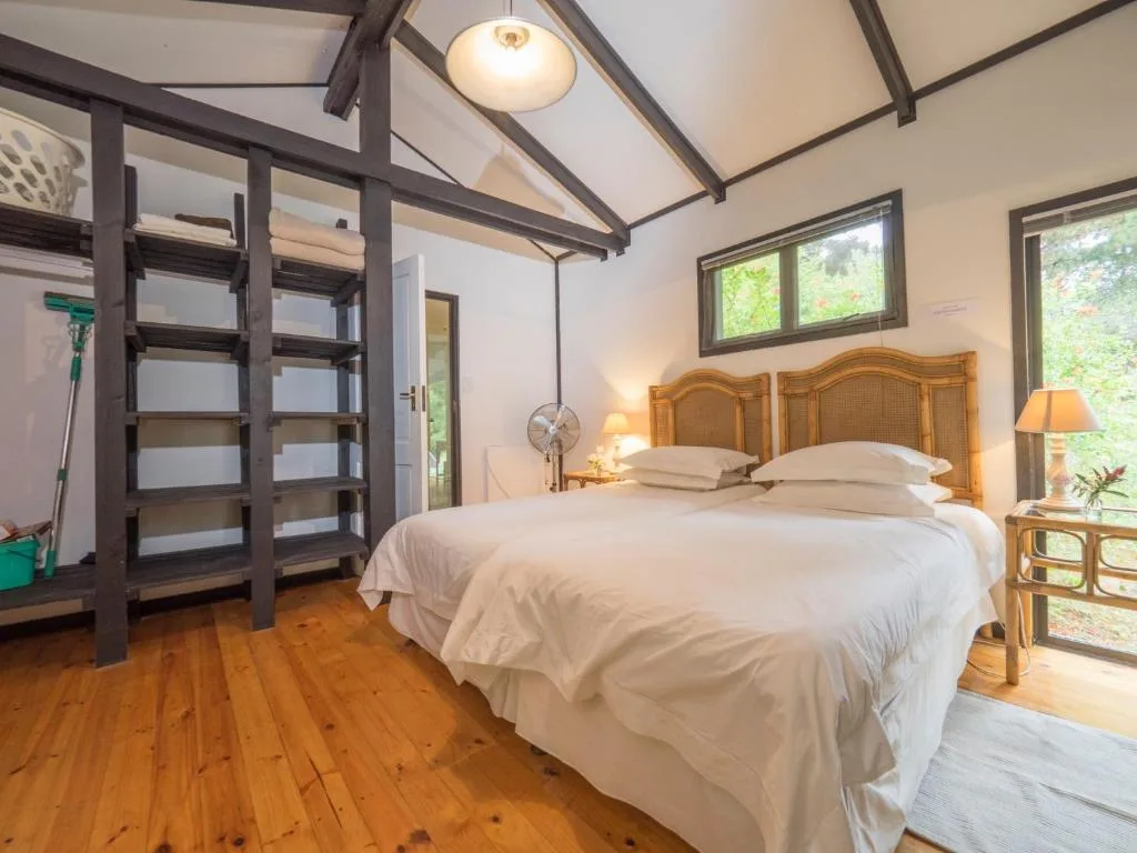 Spacious bedroom with wooden bed frame and white linens, wooden floors, beamed ceiling
