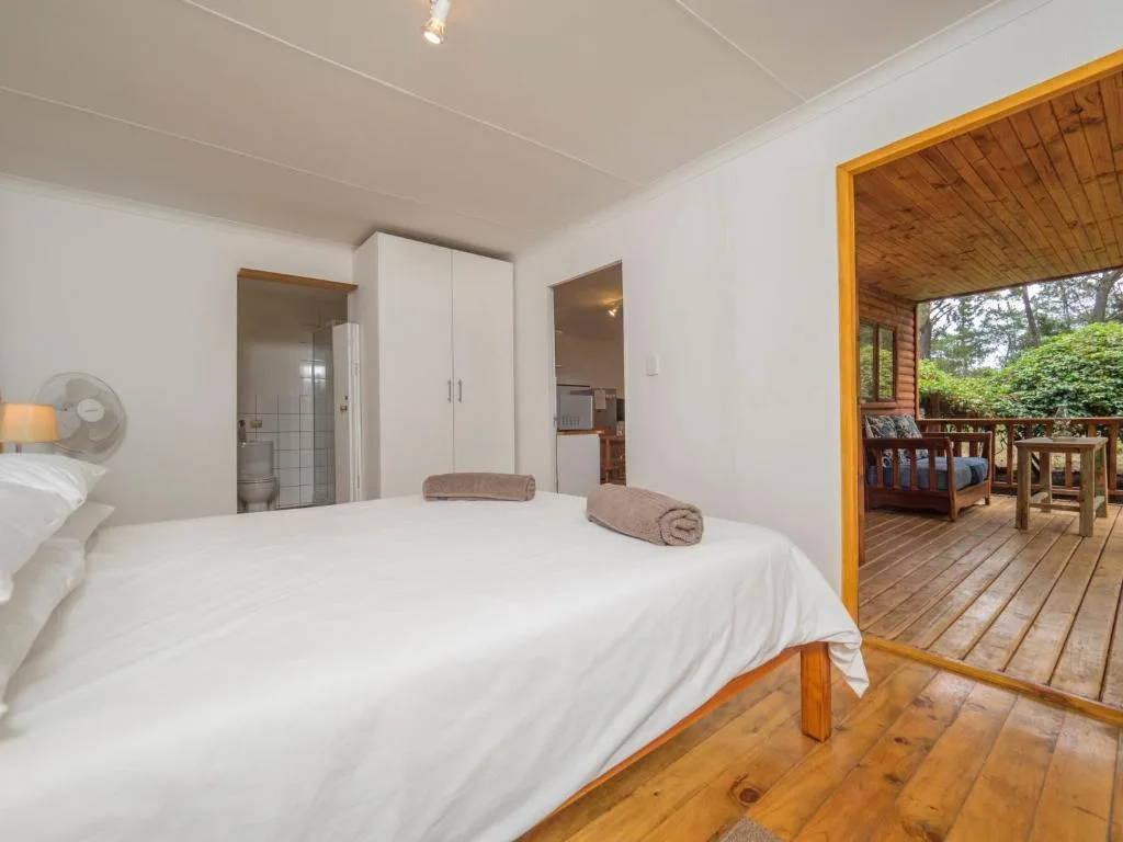 Bright bedroom with white bed, wooden floor, and deck access to garden views