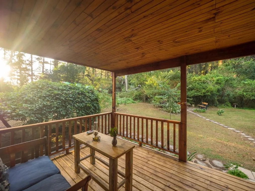 Covered wooden deck with table overlooking lush garden and forest trees