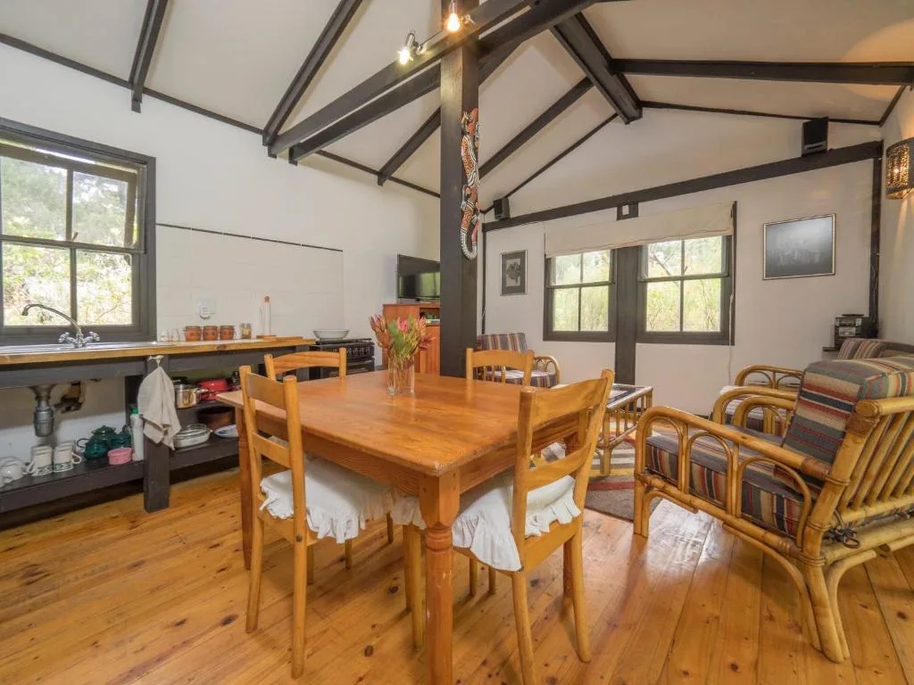 Open-plan dining and lounge area with wooden table, chairs, and exposed beam ceiling
