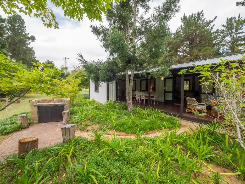 Modern cottage with deck surrounded by lush green gardens and braai area