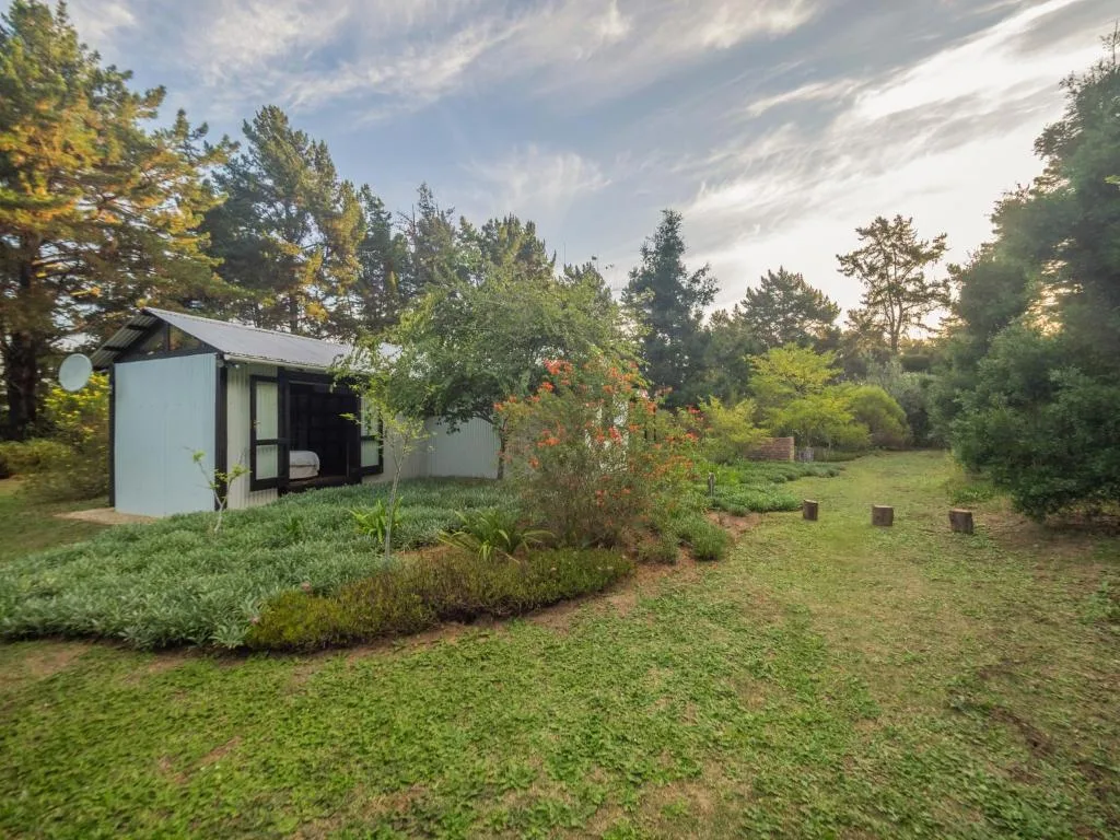 White cottage with dark trim nestled among lush gardens and trees