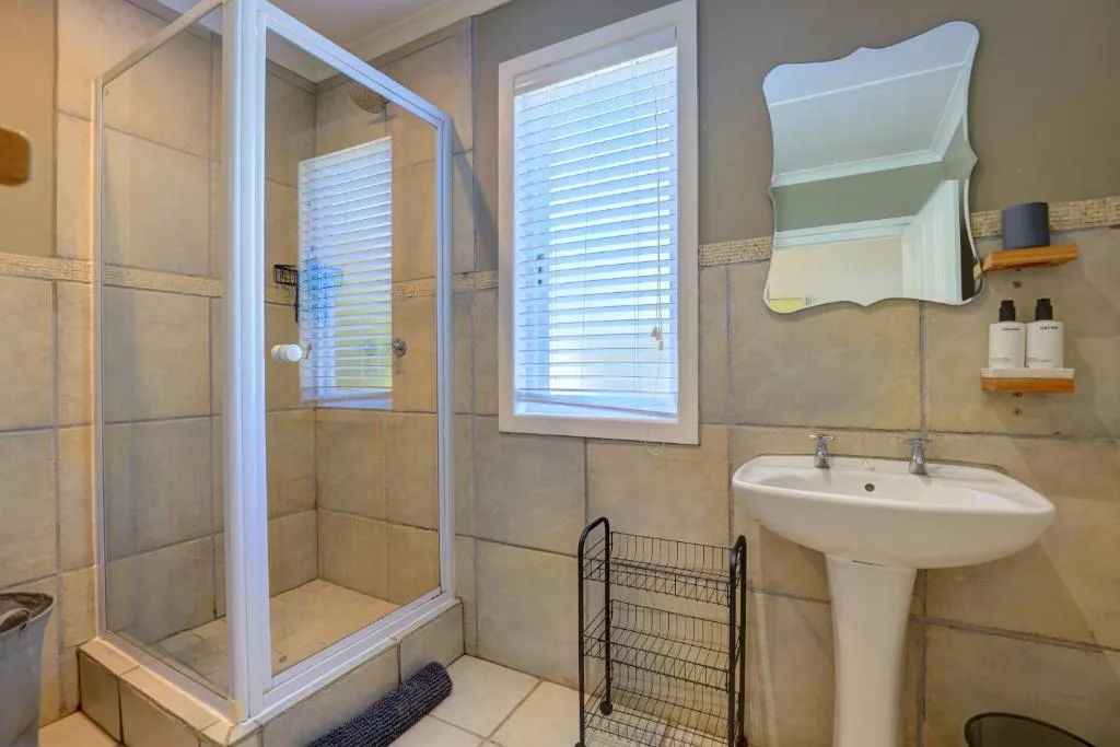 Modern bathroom with glass shower enclosure, pedestal sink, and mirror
