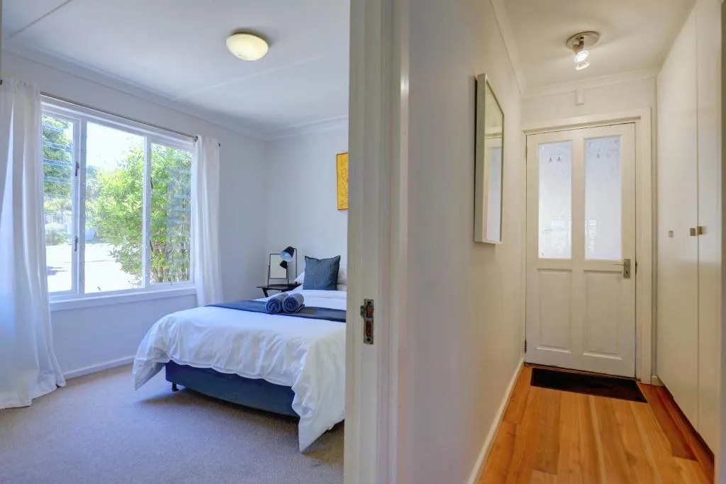 Bright bedroom with white bedding, large windows overlooking garden views