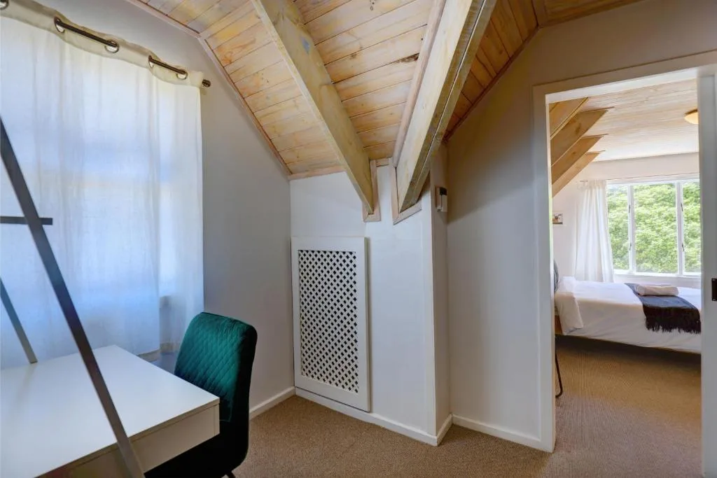 Spacious bedroom with exposed wooden beams, large windows, and garden views