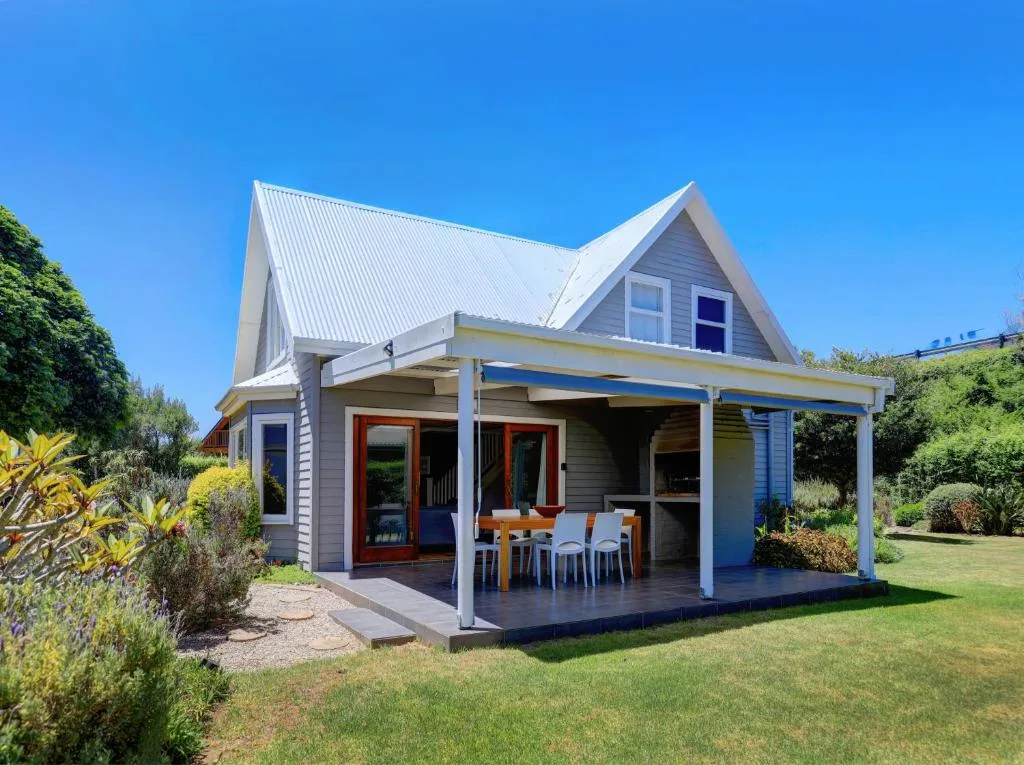 Modern cottage with white metal roof, blue exterior, and covered porch area