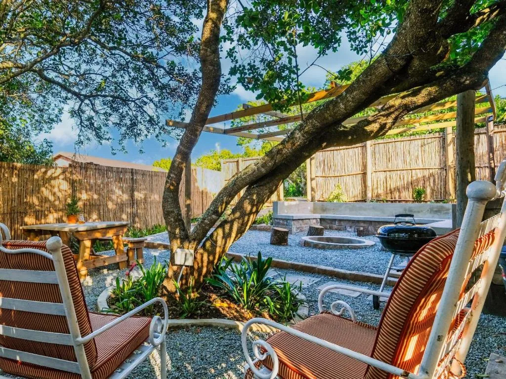 Outdoor patio with lounge chairs beneath mature tree, fire pit, braai area