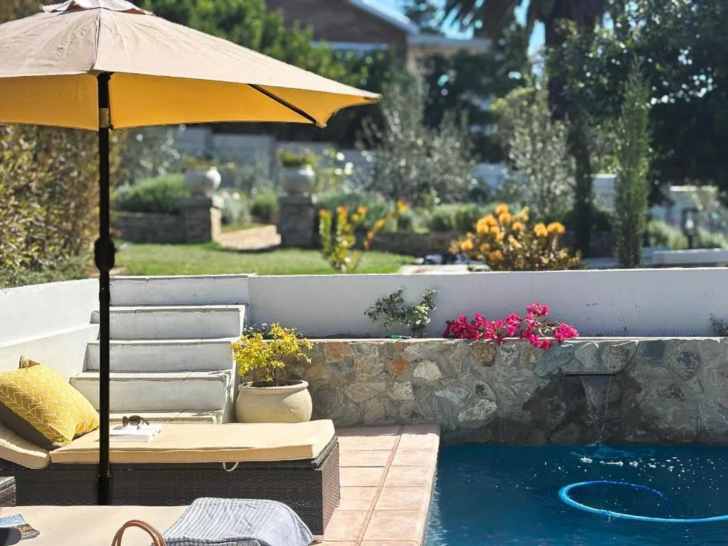 Shaded patio with yellow umbrella overlooking swimming pool and gardens