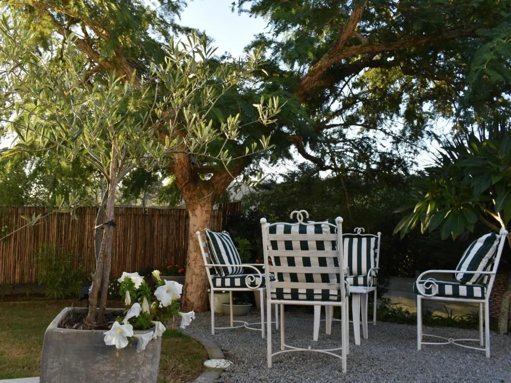 Outdoor seating area with striped chairs under mature trees and flowering planter