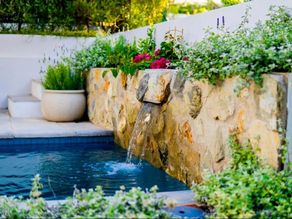 Swimming pool with natural stone waterfall feature and planted flower beds