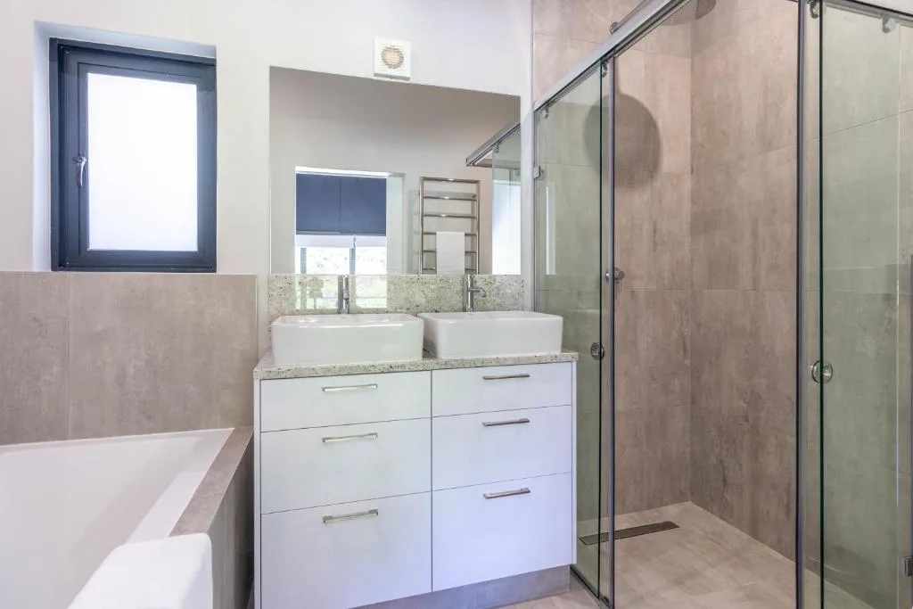 Modern bathroom with dual vanity, large mirror, and glass shower enclosure
