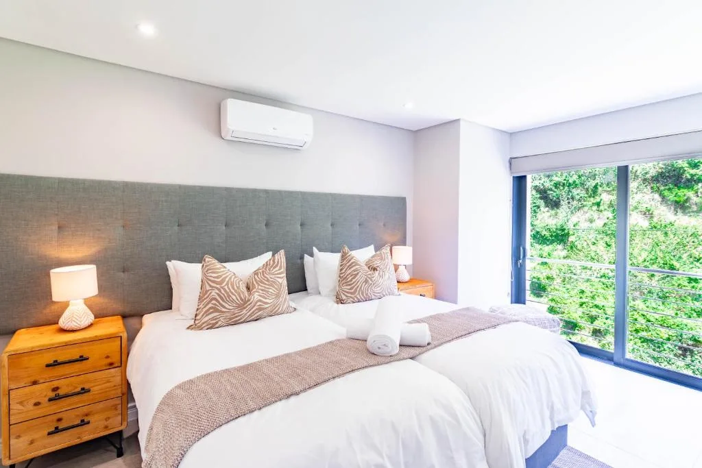 Bright bedroom with twin beds, grey headboard, and garden views through glass doors