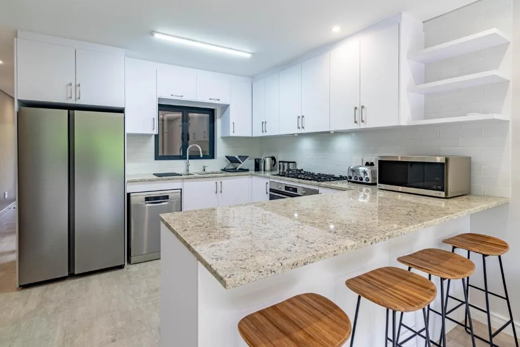 Modern white kitchen with granite countertop, stainless steel appliances, and bar seating