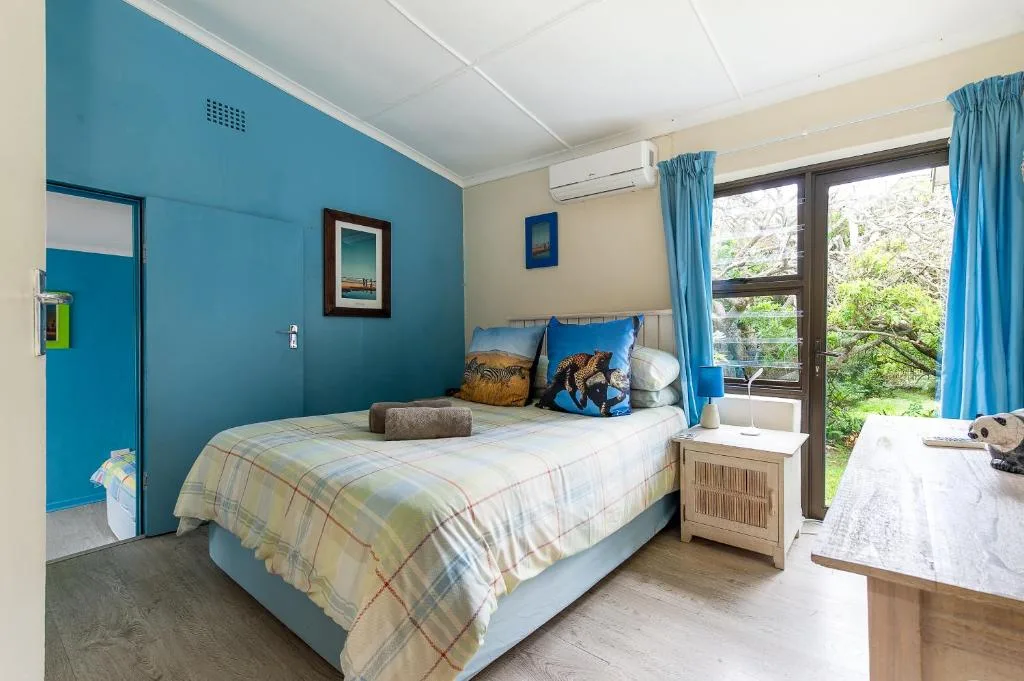 Bright bedroom with blue accent wall, queen bed, and garden views through sliding doors