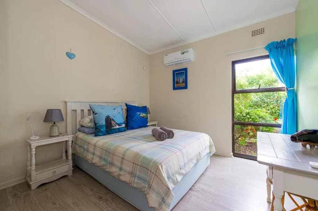 Bright bedroom with double bed, blue pillows, air conditioning unit, and garden view