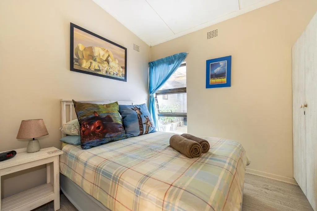 Bright bedroom with single bed, bedside lamp, framed artwork, and blue curtains