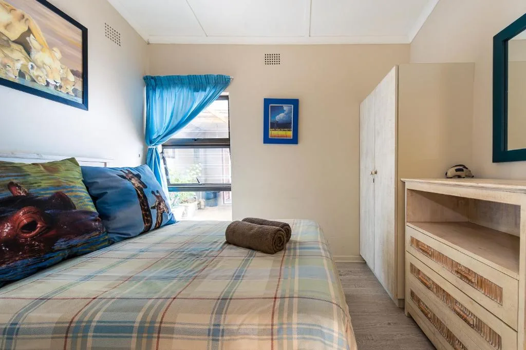 Bright bedroom with blue curtains, patterned bedding, and wooden dresser