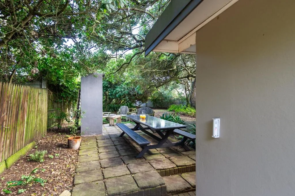 Shaded outdoor patio with picnic table and benches surrounded by trees