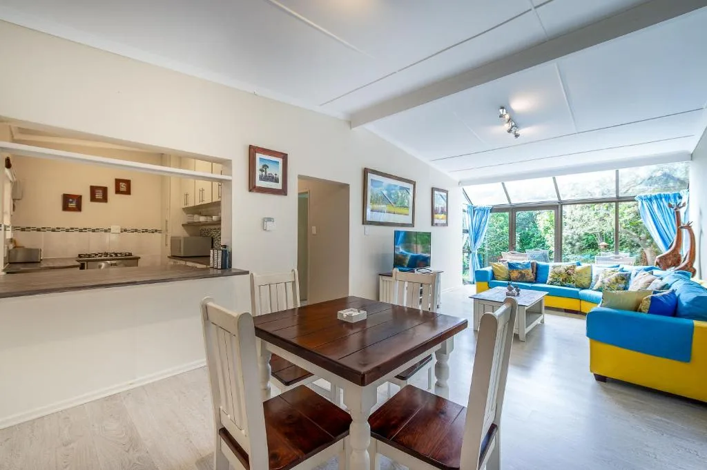 Open-plan dining area with wooden table, kitchen beyond, bright lounge visible