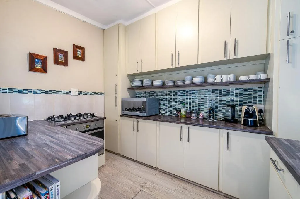 Modern kitchen with cream cabinetry, dark countertops, gas stove, and blue tile backsplash.