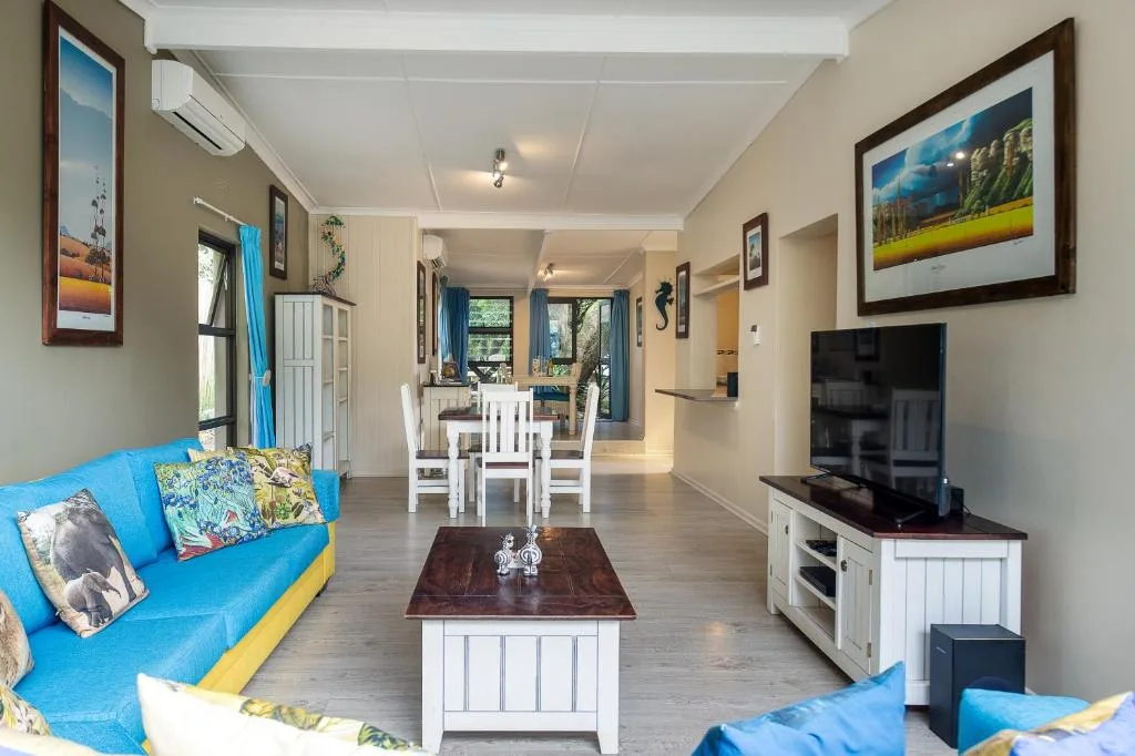 Bright open-plan lounge with blue sofas, TV, and dining area beyond