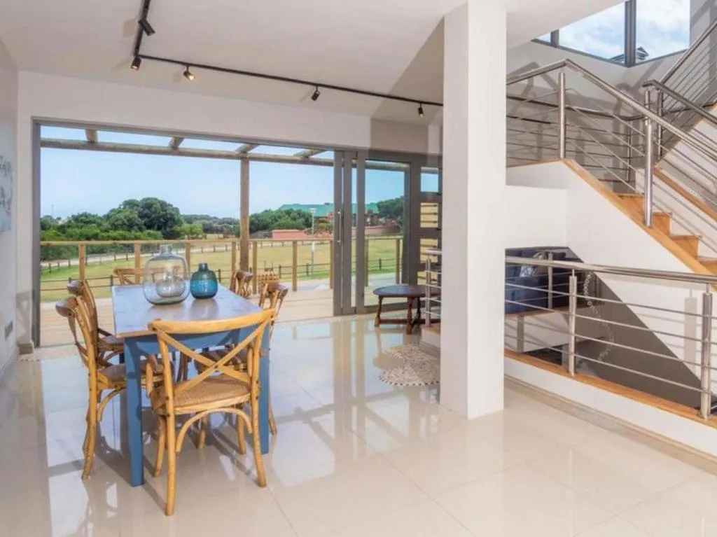 Modern dining area with blue table and wooden chairs overlooking rural landscape