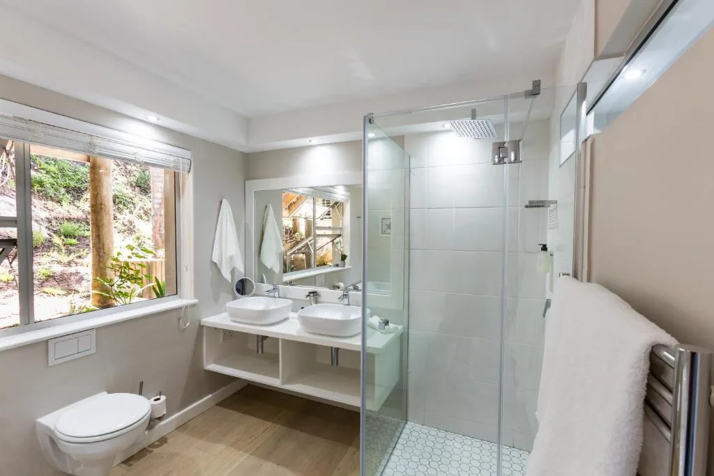 Modern bathroom with double vanity, rainfall shower, toilet, and garden view window