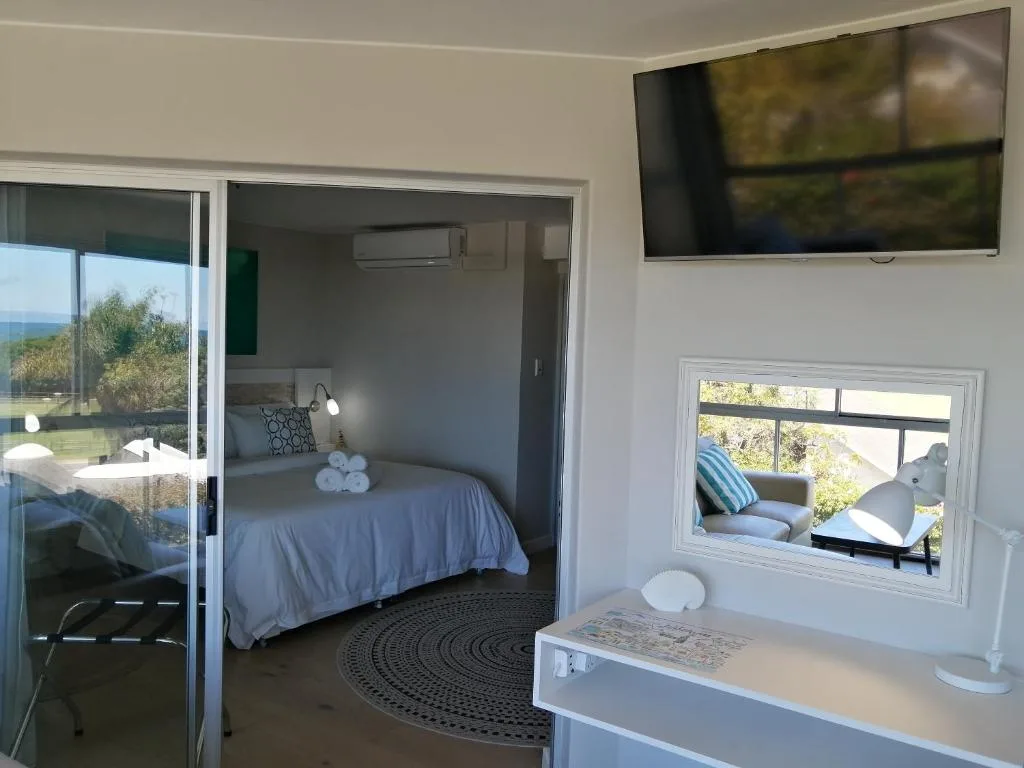Bright bedroom with double bed, TV, and ocean views through glass doors