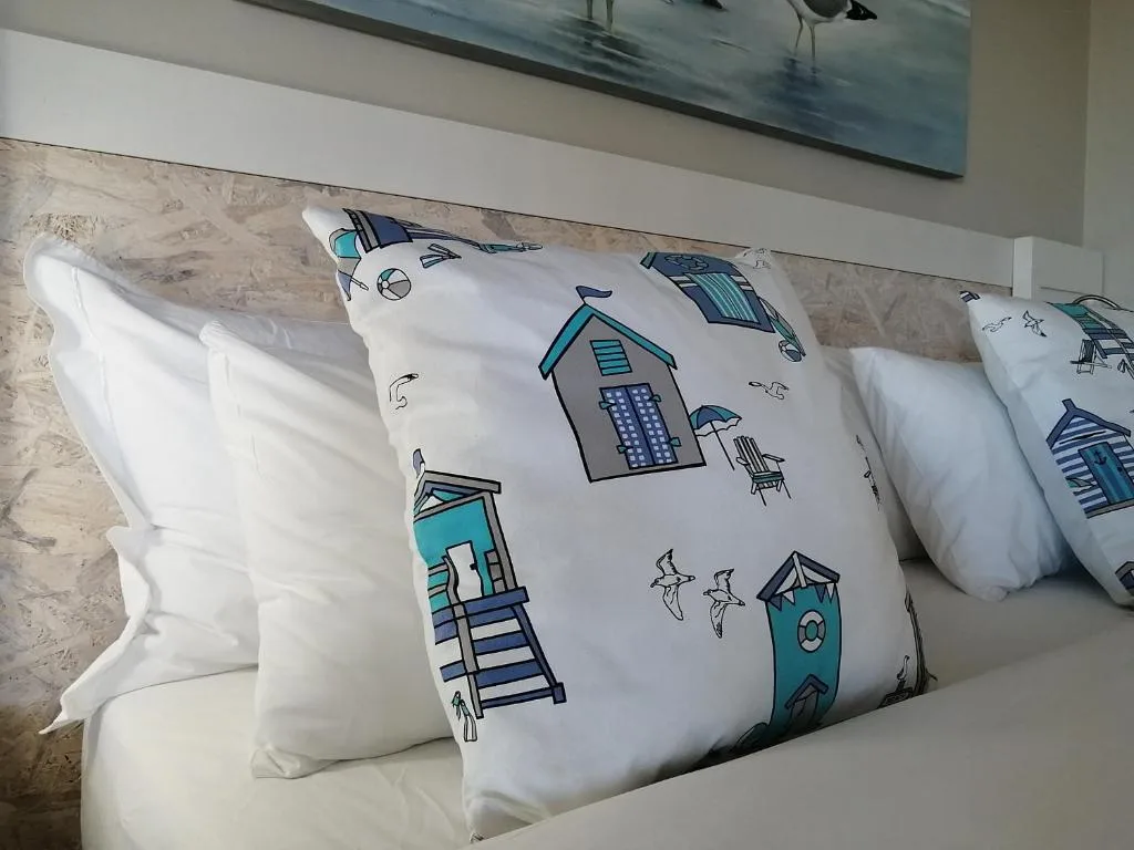 Decorative beach-themed pillows on a white bed with coastal artwork