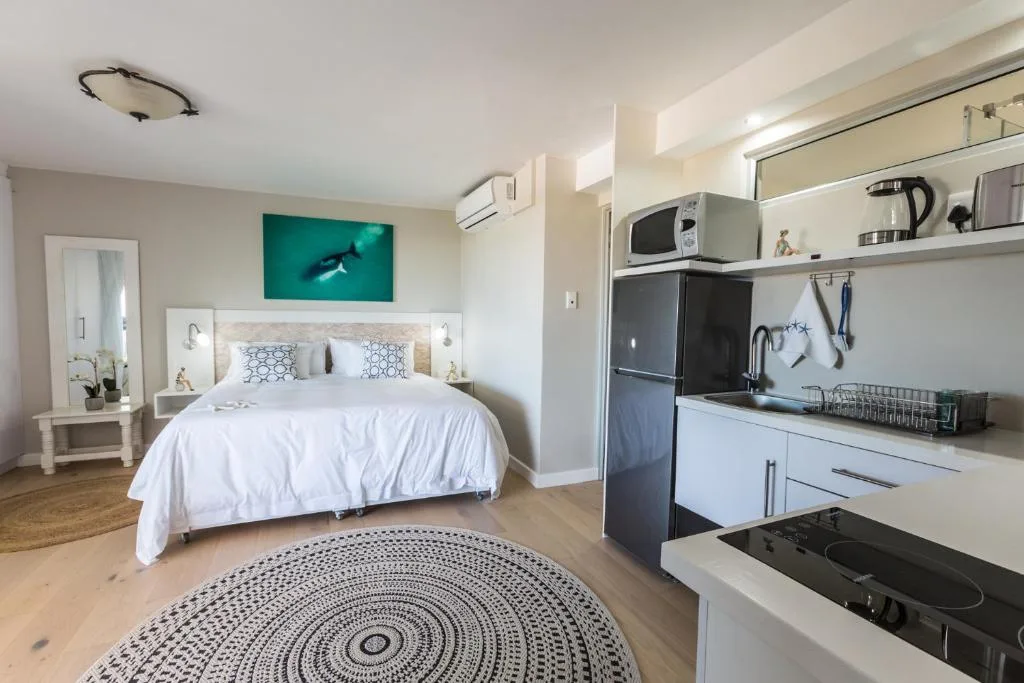 Bright studio bedroom with white bed, kitchenette, and ocean artwork