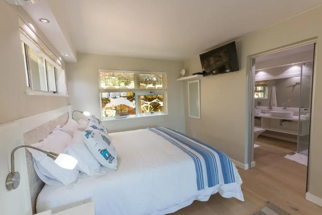 Bright bedroom with queen bed, windows overlooking garden, and ensuite bathroom visible