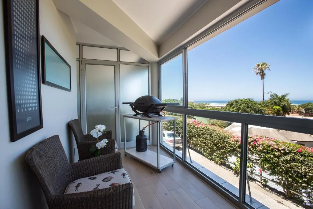 Modern balcony with ocean views, wicker seating, and flowering gardens below