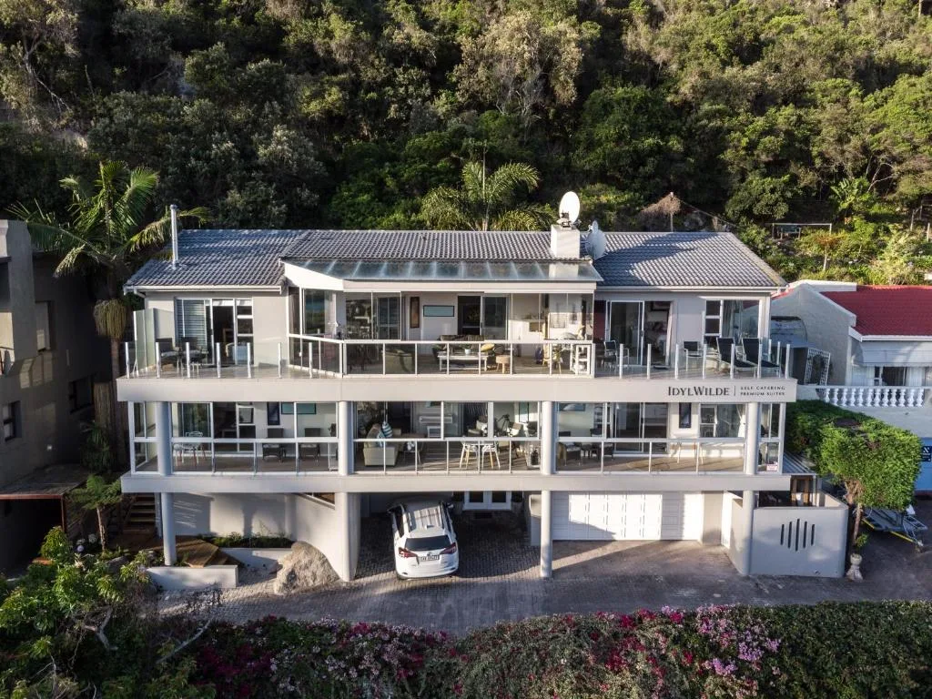 Modern white multi-story apartment building with decking and garage nestled in lush vegetation