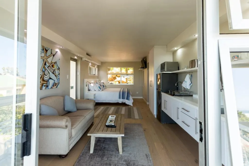 Modern open-plan lounge with sofa, coffee table, and bedroom visible beyond