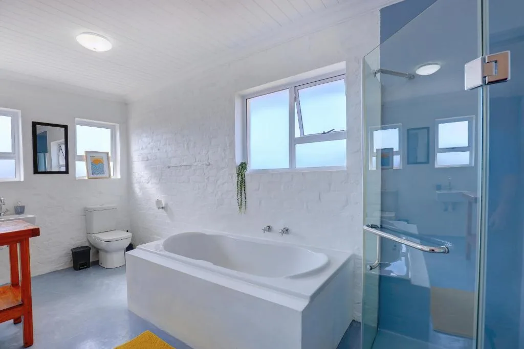 Modern bathroom with white bathtub, glass shower enclosure, and bright windows