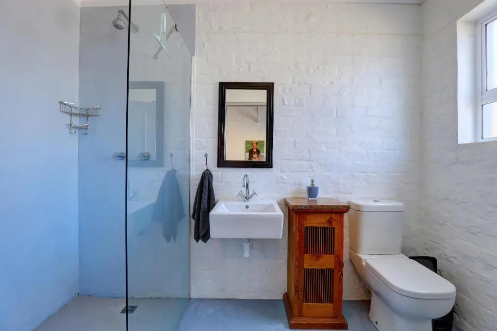 Modern white bathroom with glass shower enclosure, wall-mounted sink, and toilet