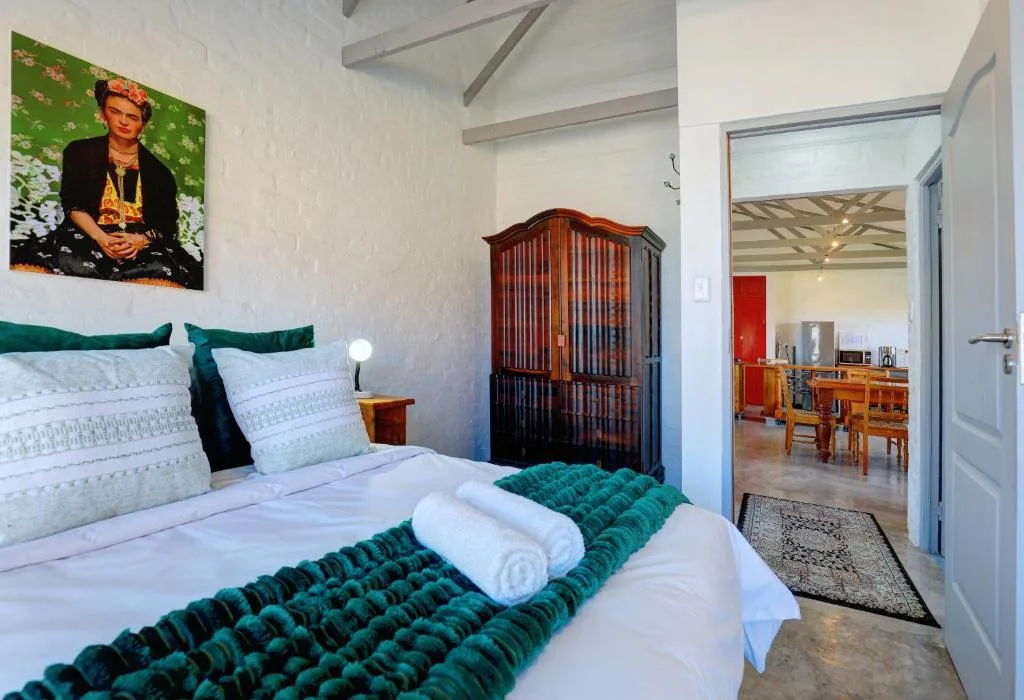 Bright bedroom with white bedding, teal accents, wooden wardrobe, and artwork