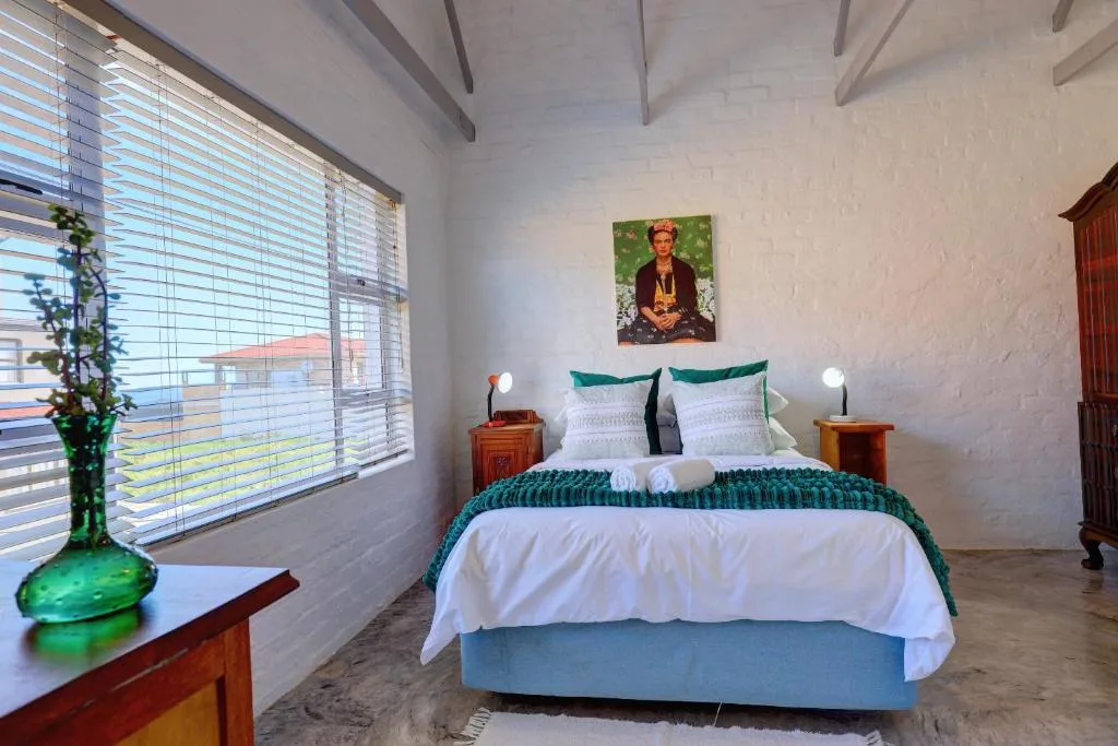 Bright bedroom with queen bed, teal bedding, wooden nightstands, and garden views