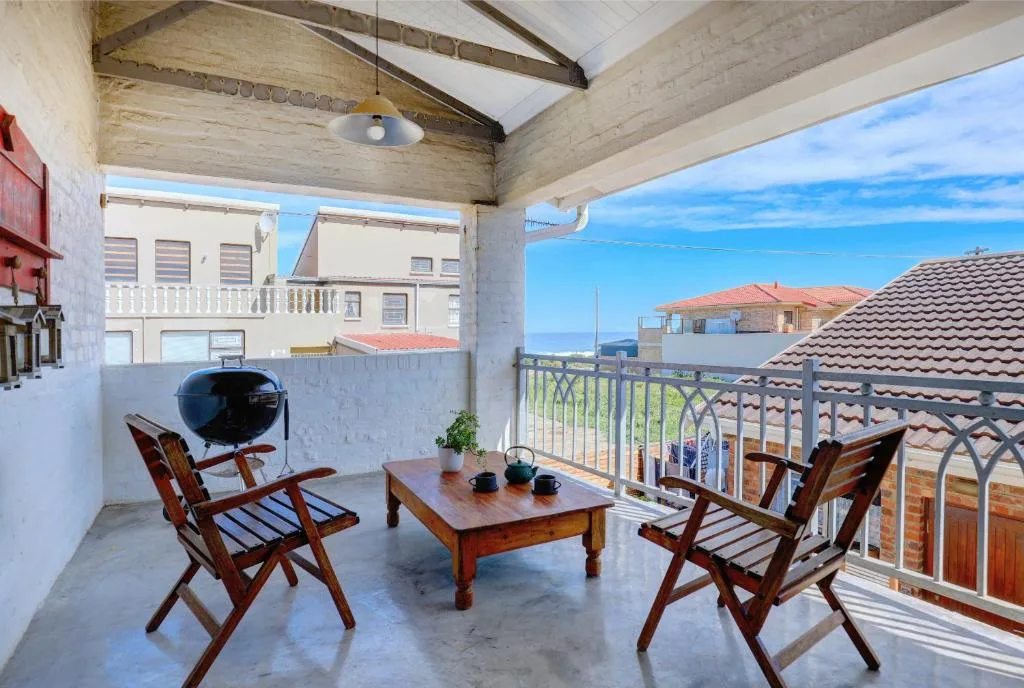 Covered patio with wooden chairs, table, and braai overlooking coastal neighbourhood