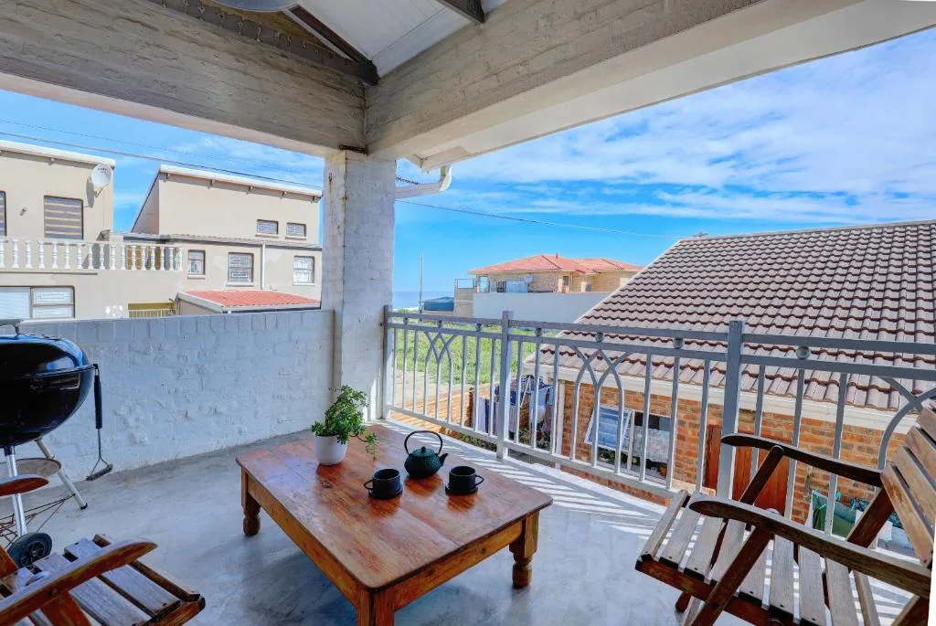 Covered outdoor patio with wooden table, chairs, and braai grill overlooking neighborhood