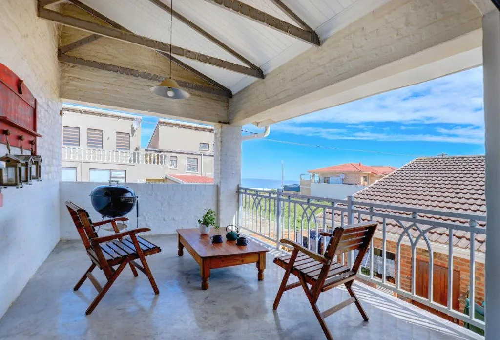 Covered patio with wooden chairs, table, and braai overlooking town